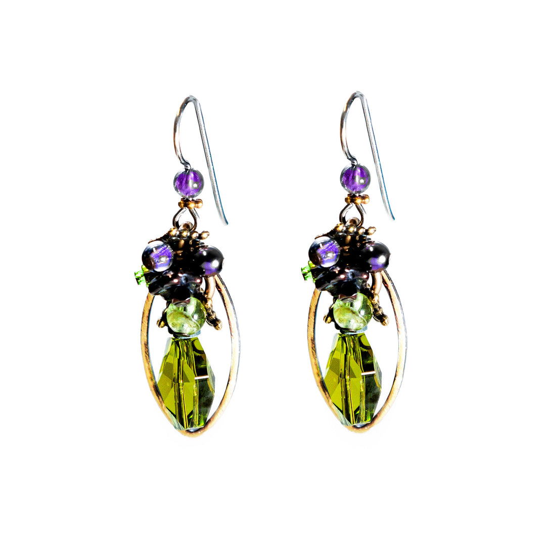 These dangle hoop earrings have been made using green Austrian crystals, amethyst and peridot gems, hand worked brass and glass beads. There is a cluster of beads made from glass, amethsyt and peridot at the top of the hooks and below them is a long, oval shaped brass hoop. There are crystals featured in the middle of the brass hoops.