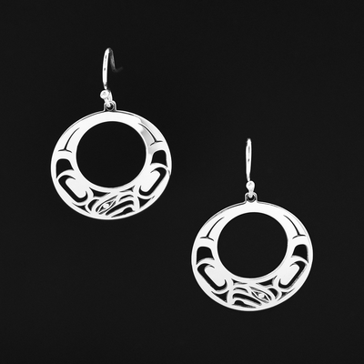 Sterling Silver Circular Offset Eagle Earrings by Grant Pauls. Each earring is in the shape of a circle. The center of it has been cutout. On the bottom of the earring the artist has cut out the profile of an eagle's head facing towards the left. The eagle has a short, pointy beak. On both sides of the eagle there are intricate designs representing the feathers and wings of the eagle.