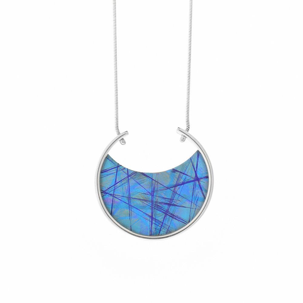 Sterling silver and blue, anodized titanium necklace. The pendant is a circular shape with the top of the circle disconnected. The anodized blue titanium is in a curved semi-circle shape at the bottom of the circle. The chain is attached through two holes at the disconnected parts of the circle.