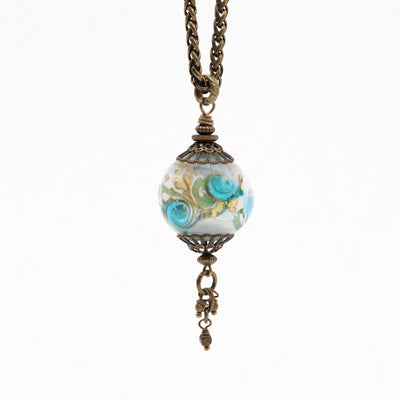 This Small Southseas Necklace is handcrafted by artist Wendy Pierson. The chain and adornments on the pendant are made from antique brass and the bead is made from her signature handmade lampworked glass. The necklace measures 29" long.