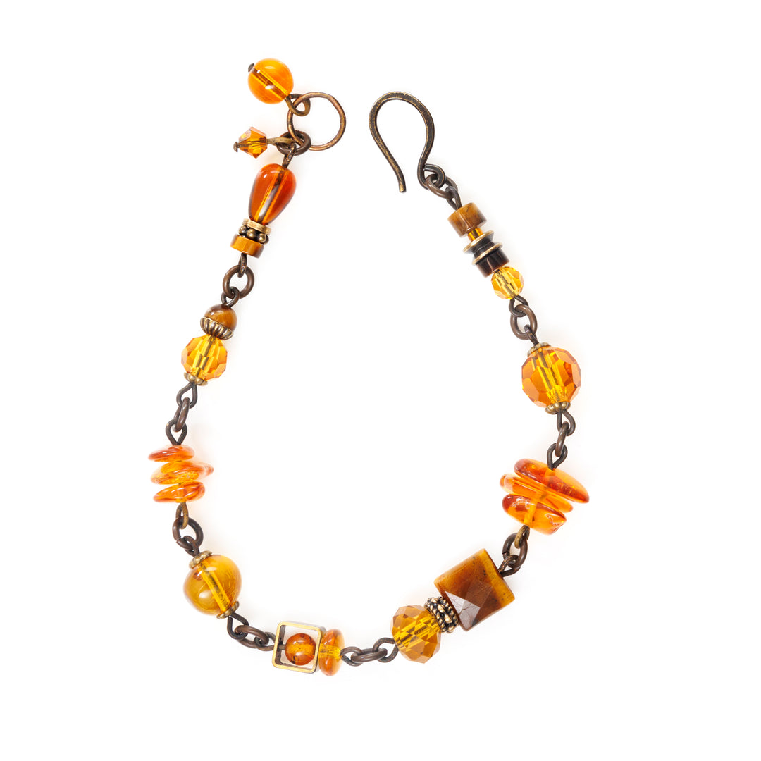This crystal bead bracelet is made from brass, Austrian crystal, Baltic amber, tiger's eye, and glass. This chain bracelet features small beads of differing materials and shaped.