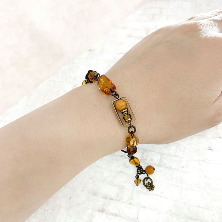 This crystal bead bracelet is made from brass, Austrian crystal, Baltic amber, tiger's eye, and glass. This chain bracelet features small beads of differing materials and shaped.
