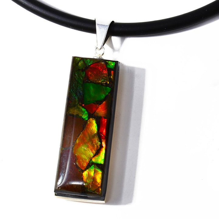 This gemstone and ivory pendant is made from sterling silver, fossilized mammoth ivory and ammolite gemstones. Pieces of the ivory and ammolite have been set into a thin, rectangular shape then set on a silver backing and bail.