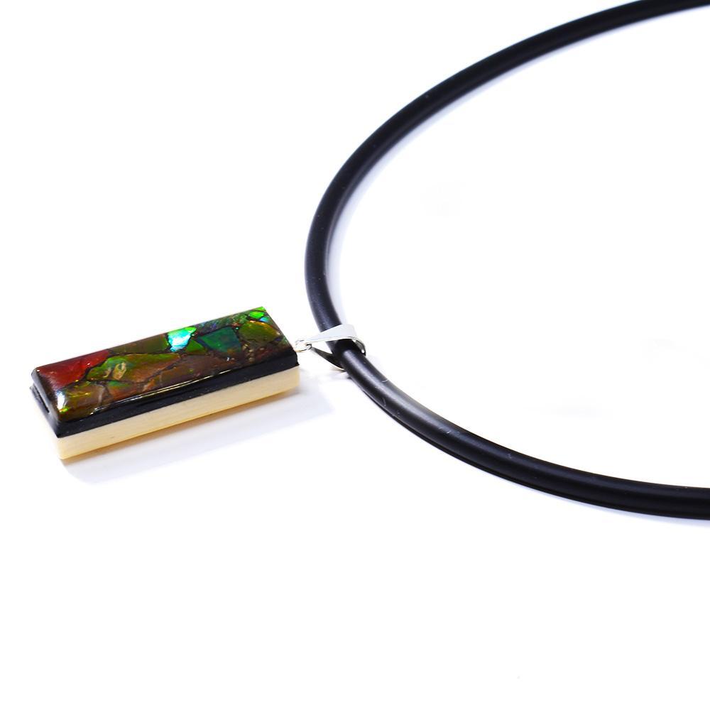 This gemstone and ivory pendant is made from sterling silver, fossilized mammoth ivory and ammolite gemstones. Pieces of the ivory and ammolite have been set into a thin, rectangular shape then set on a silver backing and bail.