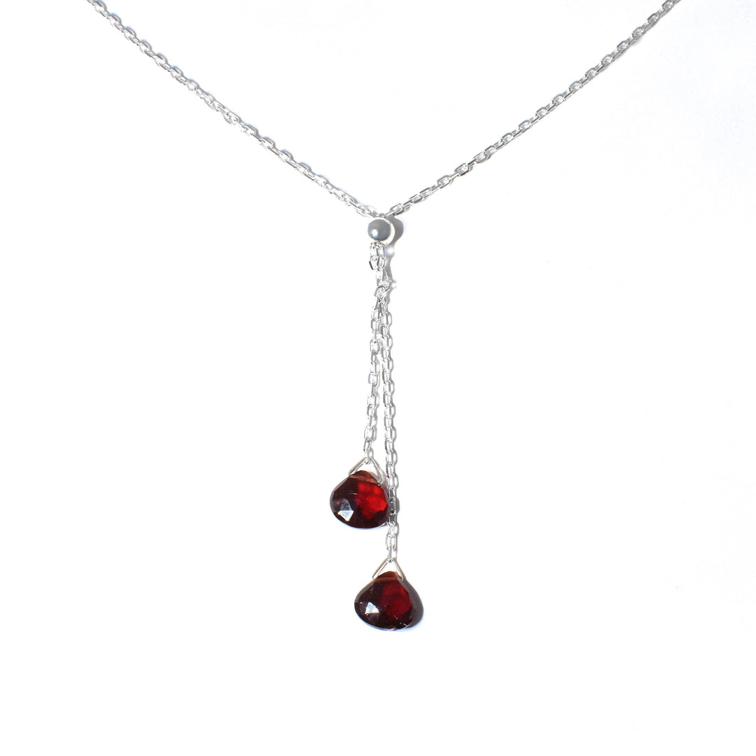 This garnet lariat necklace is made from sterling silver and genuine garnet gems. The chain is dainty and there are two lariats with garnet gems dangling from them. The gems are teardrop shaped and polished.