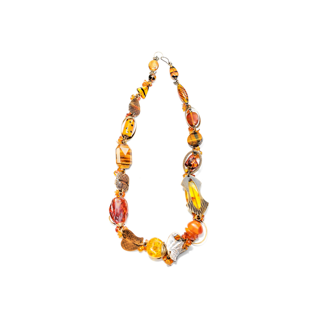 This crystal bead necklace is made from lampworked glass, mother of pearl, Austrian crystal, handworked brass, Baltic amber, tiger's eye, citrine, glass, agate, and resins. The bracelet has a chunky look and the beads have unique sizes, designs and materials. There are brass charms and designs featured around the beads.