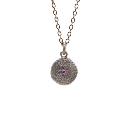 This pink tourmaline necklace is circular in shape and light grey in colour. It has a round pink tourmaline in the center with sun rays around it.