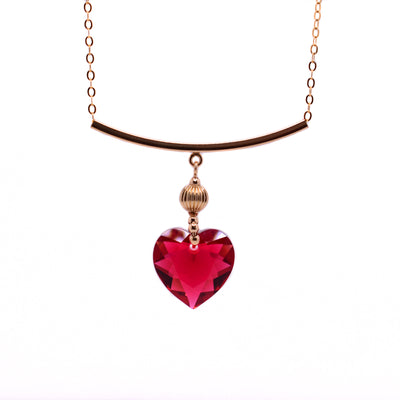 This red crystal necklace is heart-shaped and red in colour. It is connected to a gold-filled bar through a bail that has gold-filled sphere adornment.