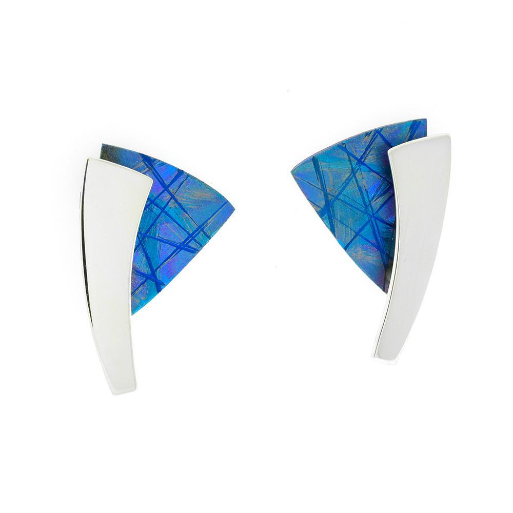These titanium stud earrings are made from sterling silver and and anodized titanium. There are triangular titanium pieces with a silver band running down the earring. The titanium pieces have been anodized to achieve the blue color and designs featured on the piece.