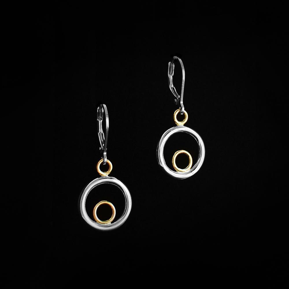 These dangle hoop earrings are made from sterling silver and 14K gold. The piece has a large silver hoop with a gold hoop in the middle of it and a small gold hoop attached to the top of the silver ring and the hooks.