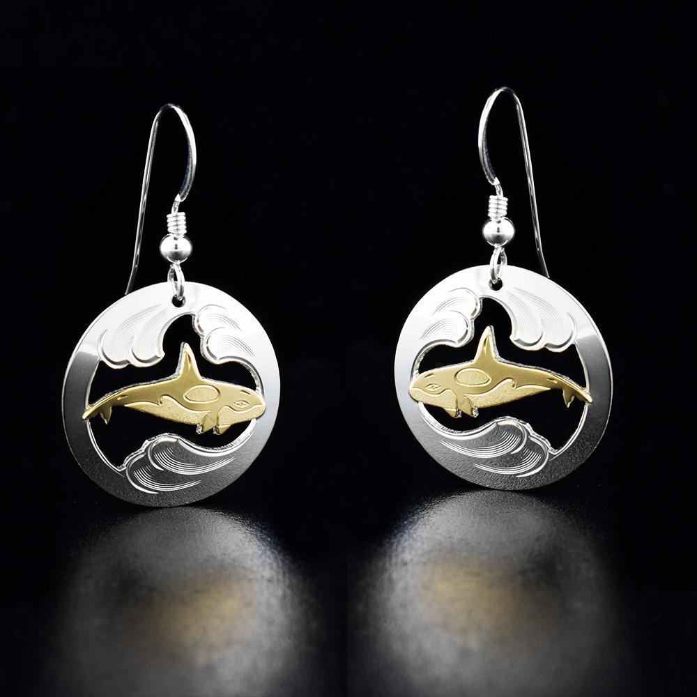 These Orca earrings are made from sterling silver and 10K gold with circle shaped hangs. There are cutouts, brushed designs and carvings on the surface of the hangs depicting an orca in the ocean.