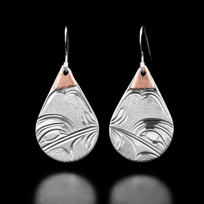 These teardrop earrings have the profile of a hummingbird head drinking from a flower in each earring. There are triangle-shaped copper accents at the top of each earring.