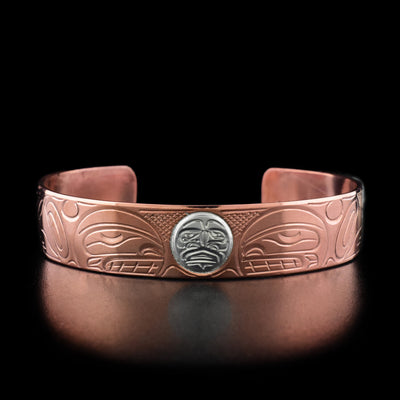 In the center of this copper bracelet is the face of a moon made from sterling silver. On both sides are the profiles of orcas facing inward.