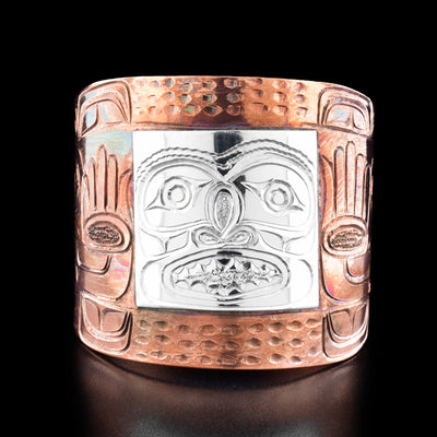 Sterling Silver and Copper 2.5" Man Bracelet by Paddy Seaweed. The design depicts the face of a man in a square shape made out of sterling silver in the center of the bracelet. The rest of the bracelet is made out of copper and intricate designs as well as two hands have been hand carved by the artist.