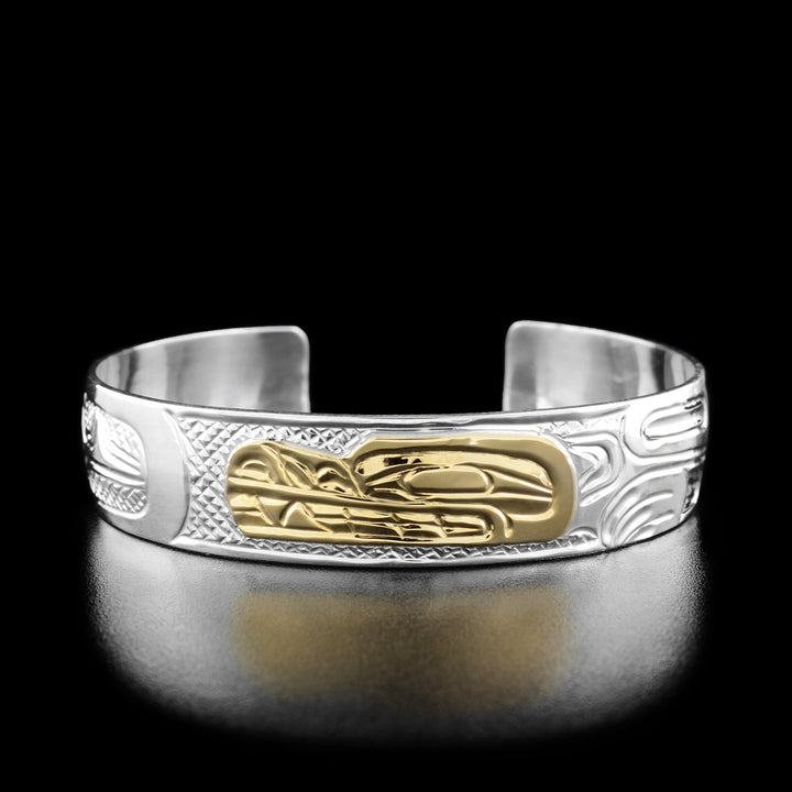 The centre of this wolf bracelet the profile of a wolf's head looking towards the left out of 14k gold. To the right of the head there is the continuation of the wolf's body including a neck, paws, and a tail all hand-carved out of sterling silver. To the left of the wolf's head the artist has hand-carved a round moon looking forward.