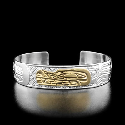 Sterling Silver and 14K Gold 1/2" Wolf and Moon Bracelet by Carrie Matilpi. In the center of the bracelet the artist has hand-carved the profile of a wolf's head looking towards the left out of 14k gold. To the right of the head there is the continuation of the wolf's body including a neck, paws, and a tail all hand-carved out of sterling silver. To the left of the wolf's head the artist has hand-carved a round moon looking forward.