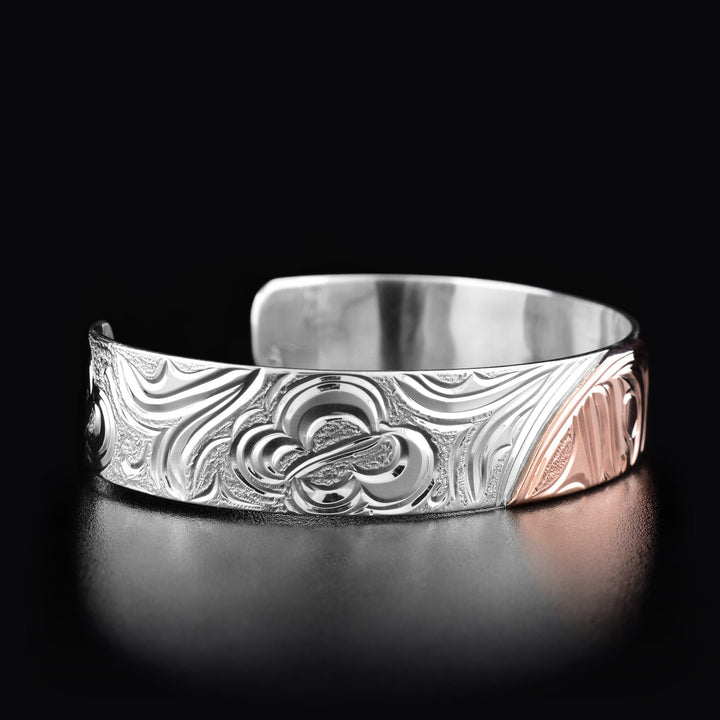 Left angle photo of the bracelet shows carved designs depicting flowers and a butterfly mid-flight.