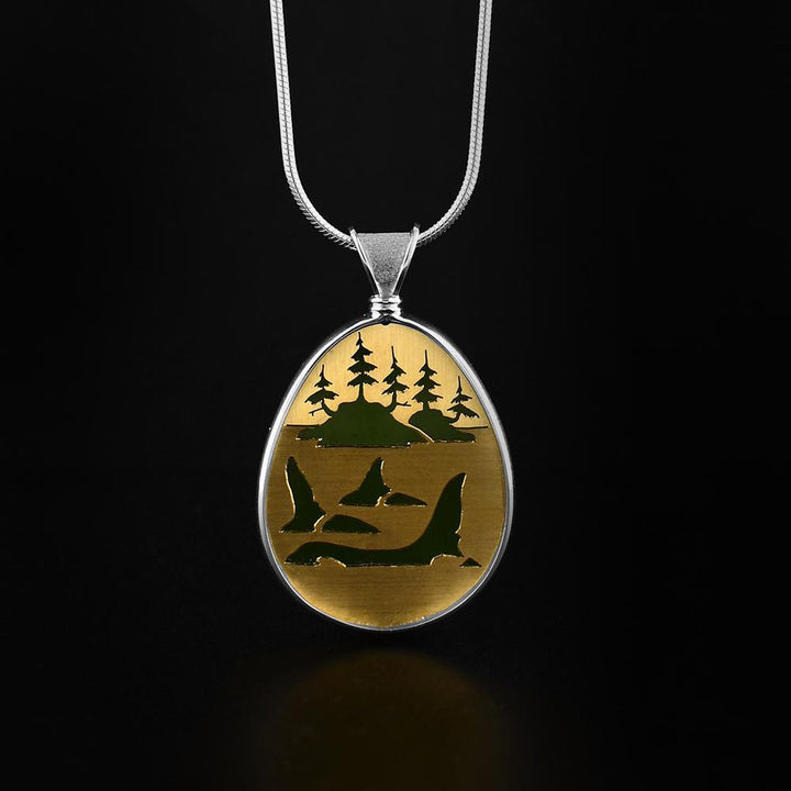 This BC jade pendant is made from 14K gold, sterling silver and A + grade BC jade. He has engraved a scene on Orcas in the ocean on a gold plate that is then set onto of the jade to give unique color to the scene. The pendant is oval shaped and the sides of it are made from silver.
