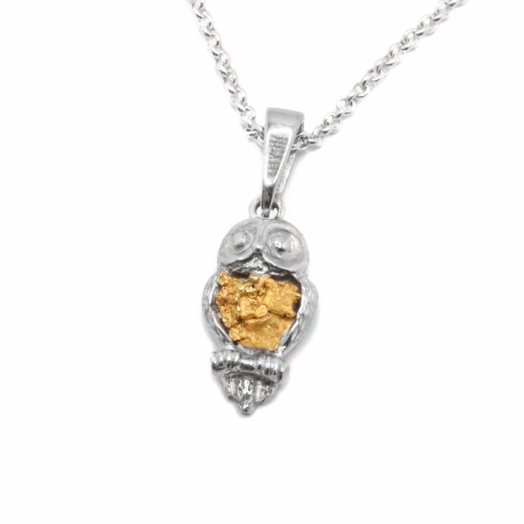 22K Gold Nugget owl pendant by Tom Gregorczyk. The pendant is in the shape of an owl looking forward with its wings tucked in to its body. The owl is displayed to be sitting on a branch. The artist has put 22k gold nuggets in the belly of the owl.
