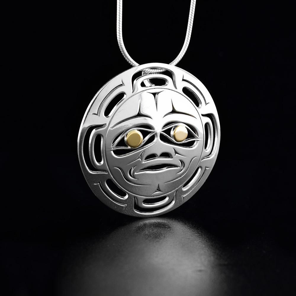 This cutout Moon pendant is made from sterling silver and 18K gold and has a circle shape. There are cutout designs made in the pendant that depict the Moon and the eyes of it are made from gold.