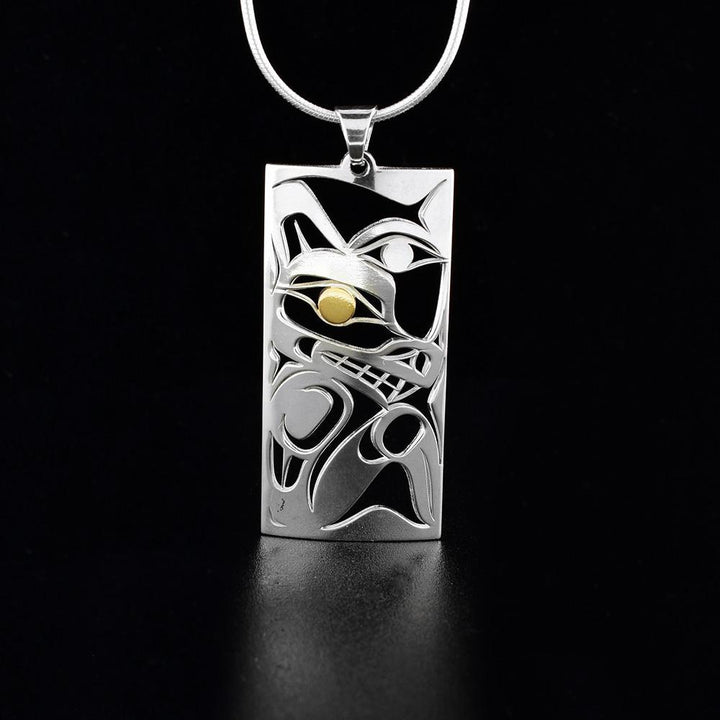 This cutout Wolf and Moon pendant has a rectangular shape and is made of sterling silver and 18K gold. There are cutout designs depicting the Wolf and the Moon. The eye of the Wolf is made from gold.