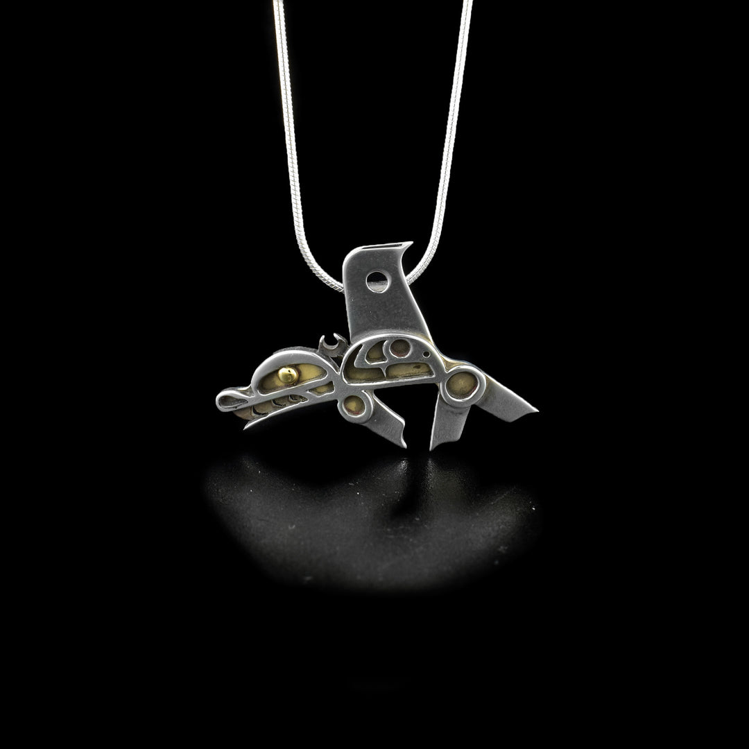 This orca pendant is in the shape of a full-body orca facing the left. The orca has a 14k yellow gold eye and an open mouth with teeth showing. The underneath layer of oxidized silver can be seen in the deep carvings of the orca's spots.