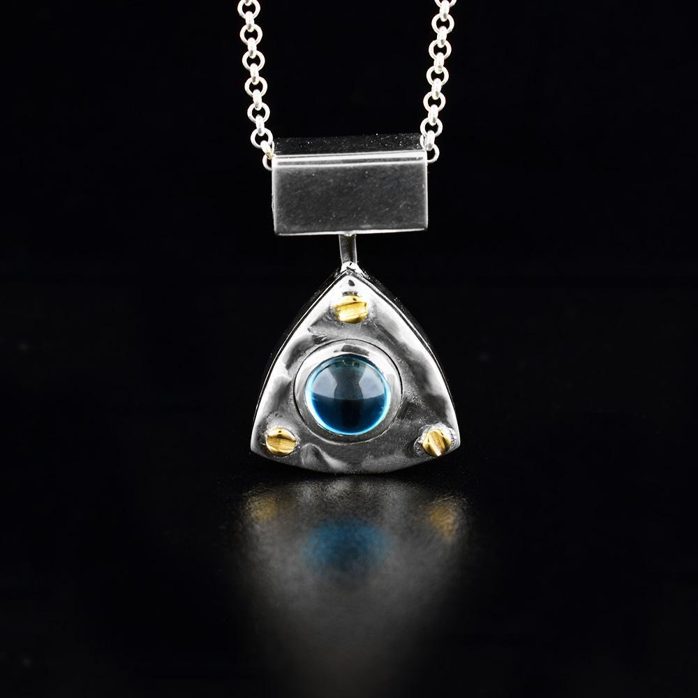 This blue topaz pendant has a dazzling blue topaz gemstone on a sterling silver pendant with 14k gold accents. The pendant is triangular and has a large, rectangular bail.