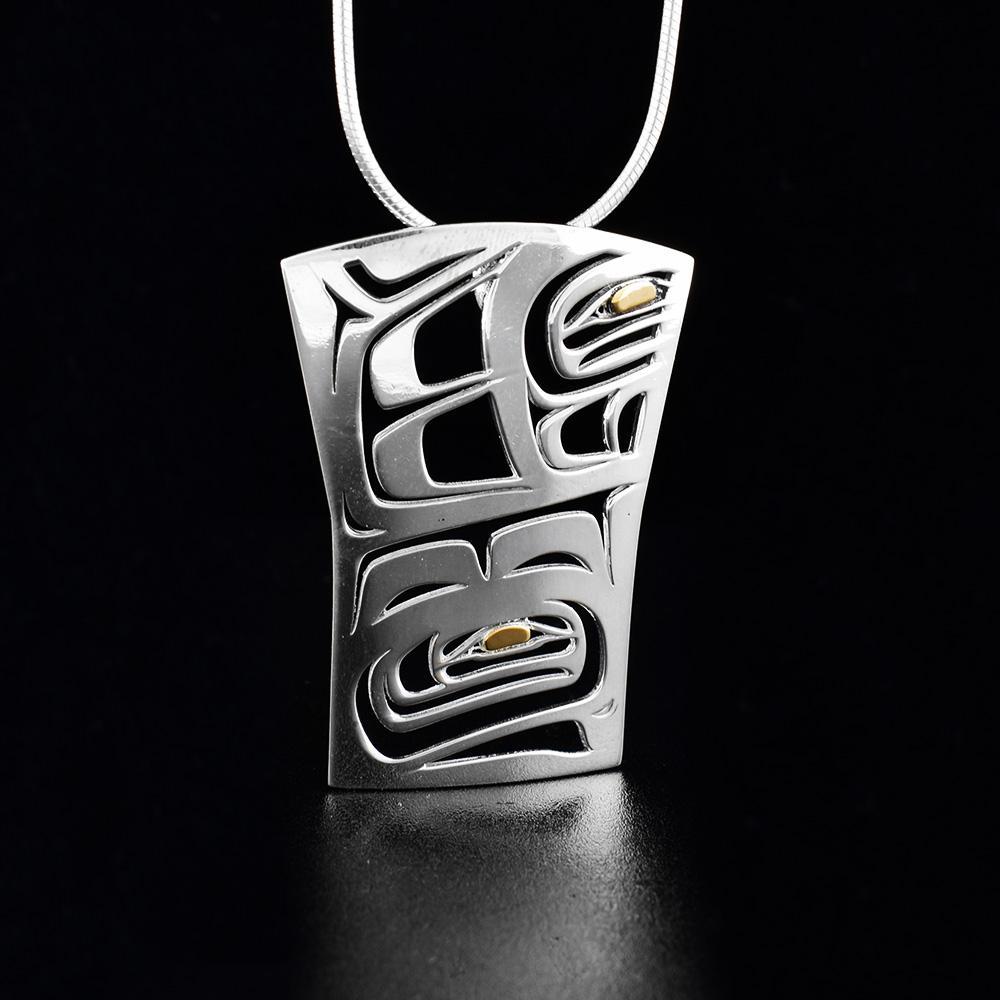 This Raven pendant is made from sterling silver and 18K gold. The pendant is large and rectangular with cutout designs depicting the Raven. The eyes of the Raven are made from 18K gold.