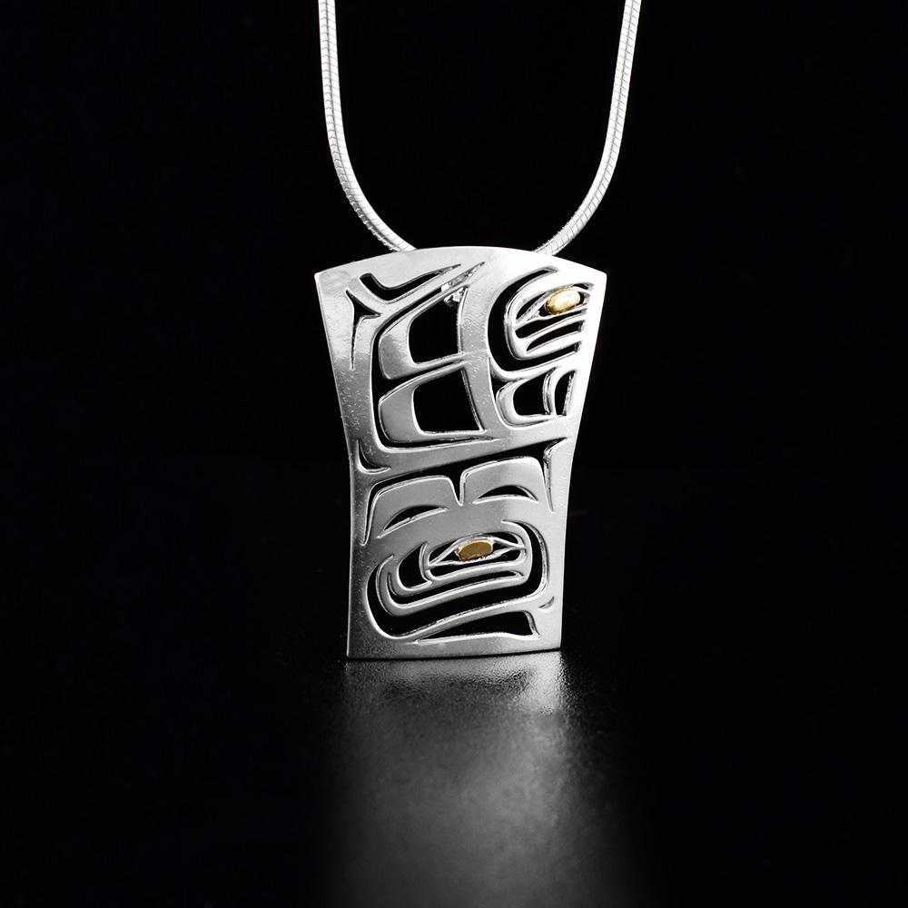 This Raven pendant is made from sterling silver and 18K gold with a rectangular shape. There are cutout designs depicting the Raven which has golden eyes.