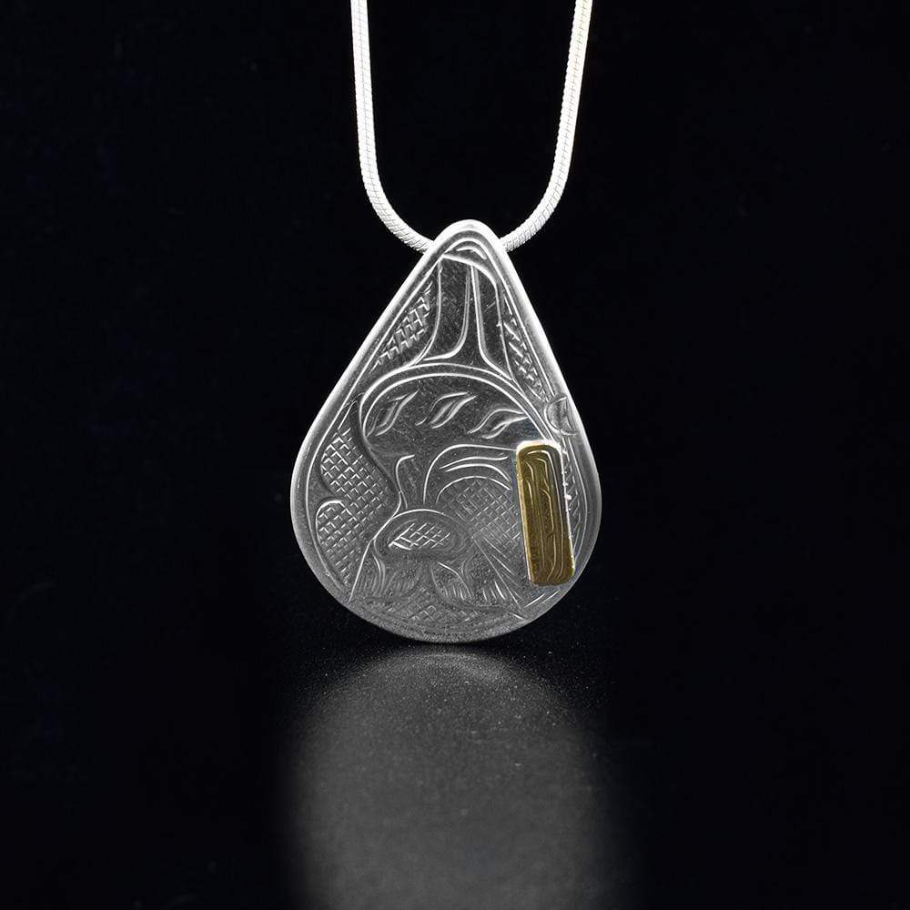 This Orca pendant is made from sterling silver and 14K gold with a large, teardrop shape. There is a depiction of the Orca and designs carved into the surface of the pendant. The Orca is made from 14K gold.