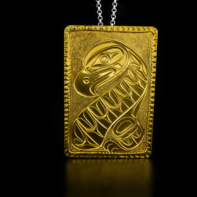 Brass Rectangle Eagle Pendant by Paddy Seaweed. The design depicts a full bodied eagle in a sitting position facing to the left with a stretched out wing facing downward. The artist has carefully hand carved the background in such a way that the body of the eagle stands out.