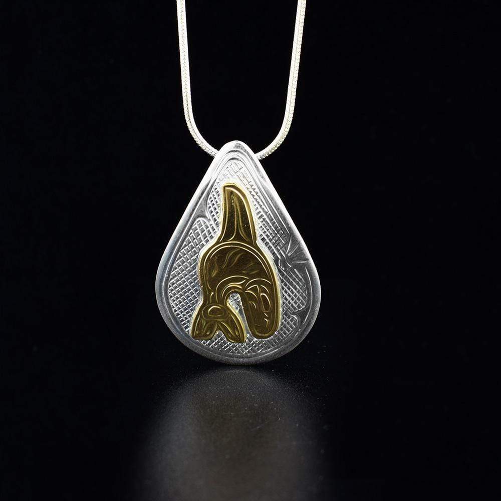 This Orca pendant is made from sterling silver and 14K gold with a large, teardrop shape. There is a depiction of the Orca and designs carved into the surface of the pendant. The Orca is made from 14K gold.