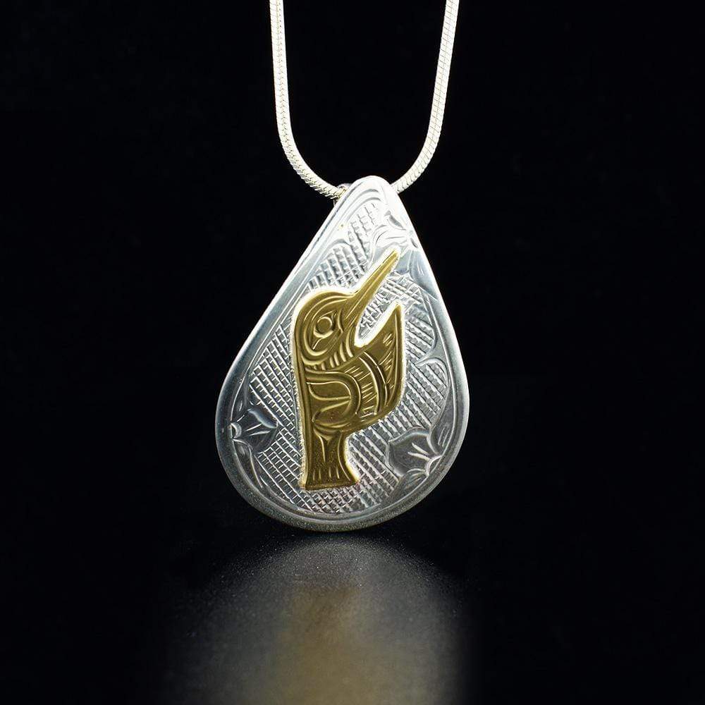 This Hummingbird pendant is made from sterling silver and 14K gold with a large, teardrop shape. There is a depiction of the Hummingbird and designs carved into the surface of the pendant. The Hummingbird is made from 14K gold.