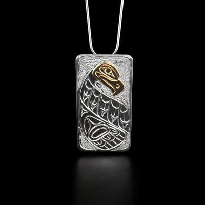 Sterling Silver and 14K Gold Rectangular Eagle Pendant by Paddy Seaweed. The design depicts a full bodied eagle facing the right. The head of the eagle is looking slightly downwards and is made from 14K gold. Under the head is the eagle's large wing spread out. The background has been delicately hand carved to allow for the eagle to stand out.