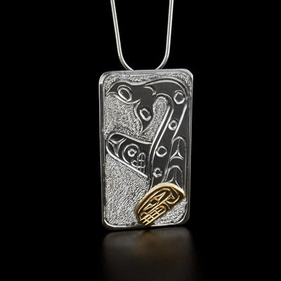 Sterling Silver and 14K Gold Rectangular Pendant by Paddy Seaweed. The design depicts the profile of a full bodied orca upside down. The head of the orca, made from 14K gold, is at the bottom of the pendant looking downward. The body of the orca is above the head with the tail curving upwards at the very top of the pendant. The artist has included intricate designs along the body of the orca. The background has been neatly hand carved to allow for the image of the orca to stand out.
