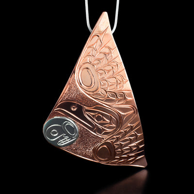 Copper Raven and Moon Triangle Pendant by Paddy Seaweed. The design depicts a raven mid flight, made out of copper, facing towards the left. Right underneath the beak of the raven is a moon's face made out of sterling silver. The background has been neatly carved to allow for the legends to stand out.
