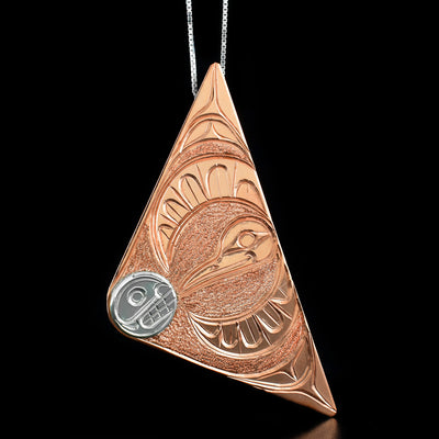 Copper Hummingbird and Moon Triangle Pendant by Paddy Seaweed. The design depicts the profile of a moon's face, made out of sterling silver, facing towards the hummingbird. The hummingbird, made out of copper, has both wings open as if mid flight and is facing the moon.