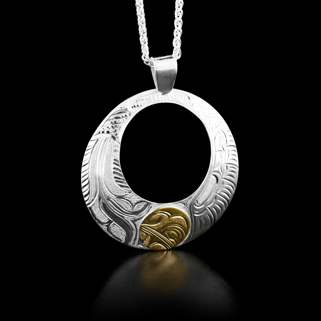 This hummingbird necklace is circular in shape and has a small cut-out hole in the top center. There is a gold circle at the bottom of the pendant with the head of a hummingbird in it. The rest of the piece is carved with flowers and feathers.