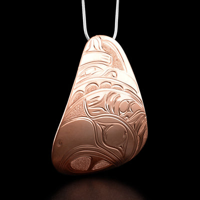 This copper necklace is teardrop shaped and has an eagle's head facing the left at the bottom and a raven's head facing the right at the top.
