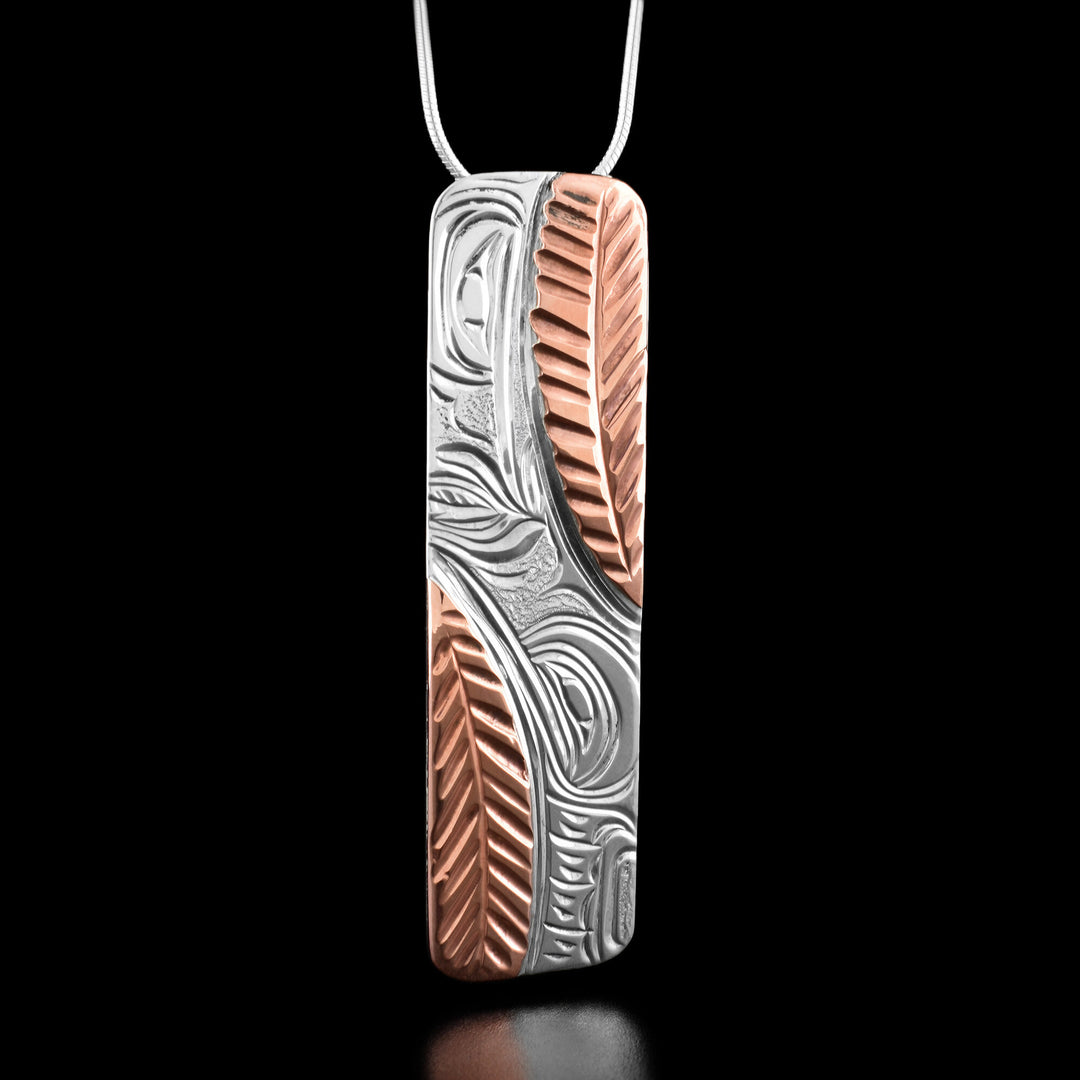 This hummingbird pendant has the profile of two hummingbirds facing each other on the top and bottom. There are copper accents in the shape of feathers on two corners of the pendant.