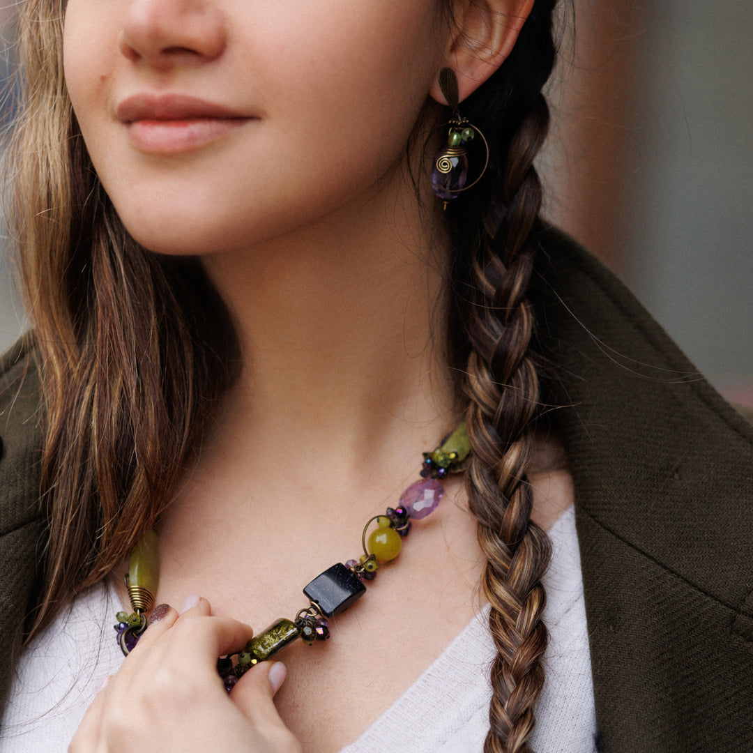 Young woman with brown hair and olive-toned skin wearing Honica's Mystic necklace. Boho statement necklace with glass beads, amethyst, jade, and brass. Handmade in Canada.