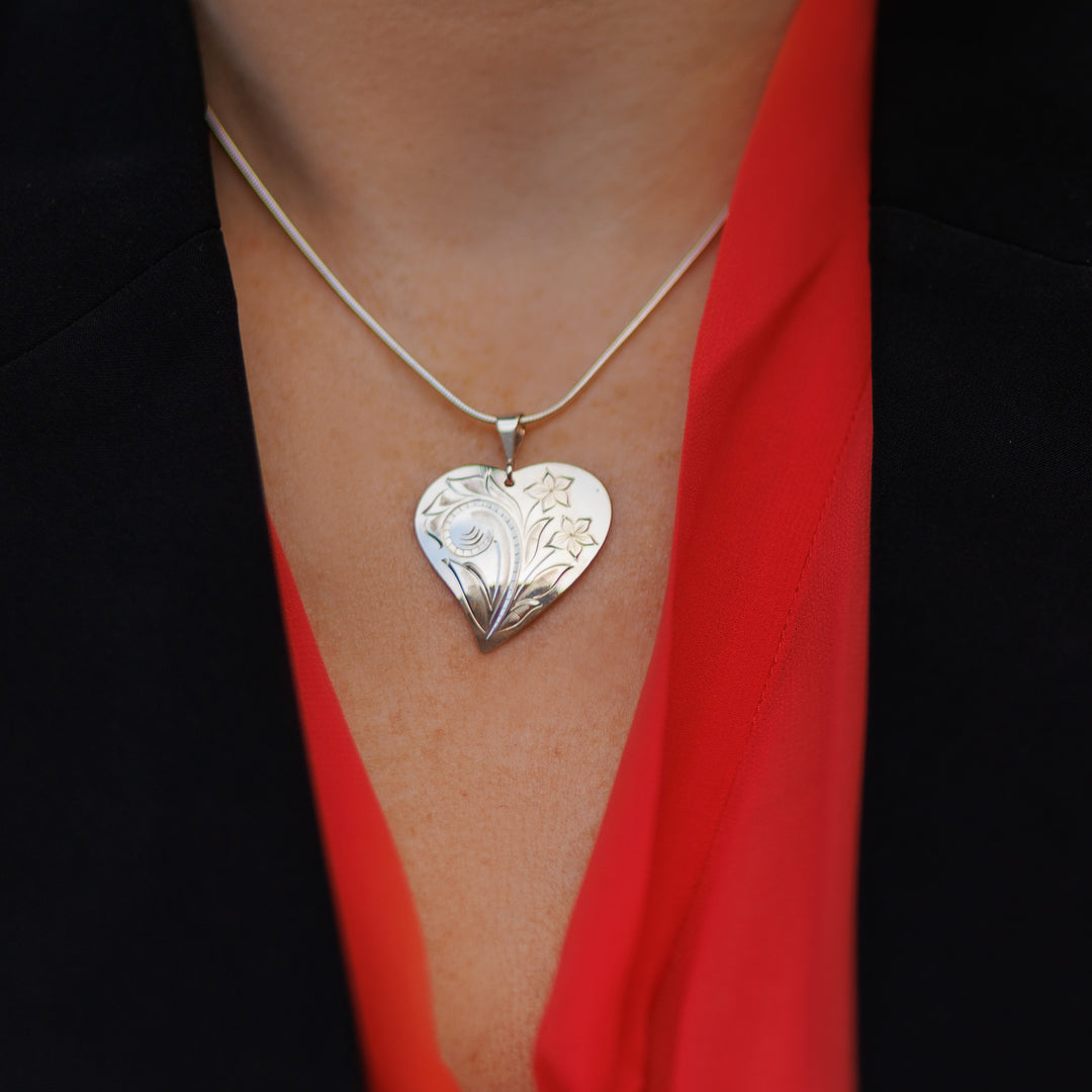 This sterling silver heart pendant necklace has intricate carvings on the surface of it depicting flowers.