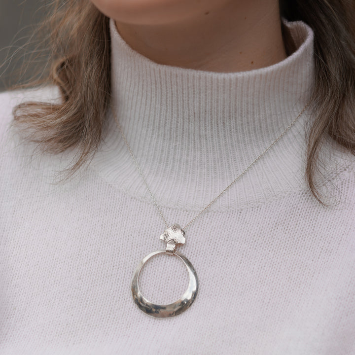 This sterling silver, hollow pendant is a large, tapered hoop attached to a decorative bail. There is a snake skin textured pattern on the surface of the bail.
