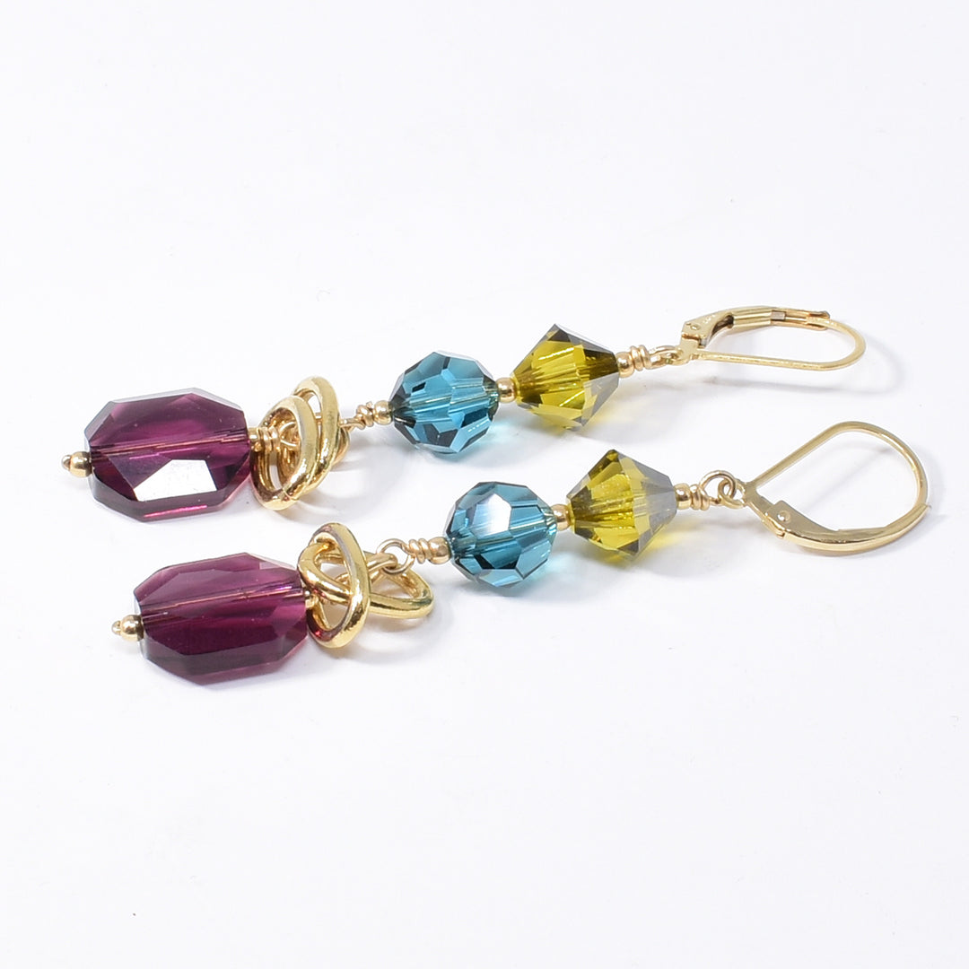 Dazzling Blue, Green and Purple Swarovski Crystal Earrings handcrafted by artist Karley Smith. She has used Swarovski Crystal and gold-plated adornments and wire to create the earrings. The Swarovski crystals are in the colours: Indicolite Satin, Lime Satin and Amethyst. Ear hooks are gold-filled. Each earring measures 2.50" x 0.40" including hook.