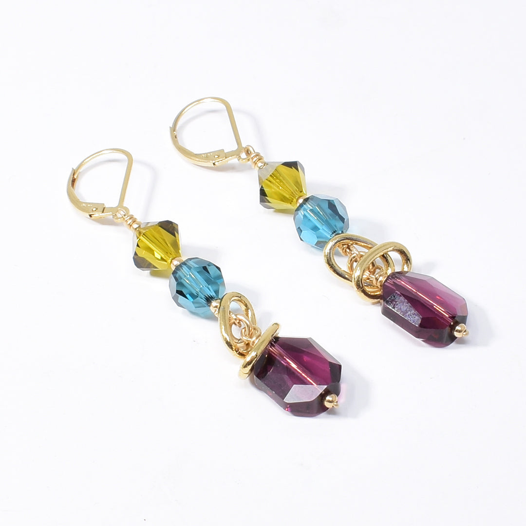 Dazzling Blue, Green and Purple Swarovski Crystal Earrings handcrafted by artist Karley Smith. She has used Swarovski Crystal and gold-plated adornments and wire to create the earrings. The Swarovski crystals are in the colours: Indicolite Satin, Lime Satin and Amethyst. Ear hooks are gold-filled. Each earring measures 2.50" x 0.40" including hook.