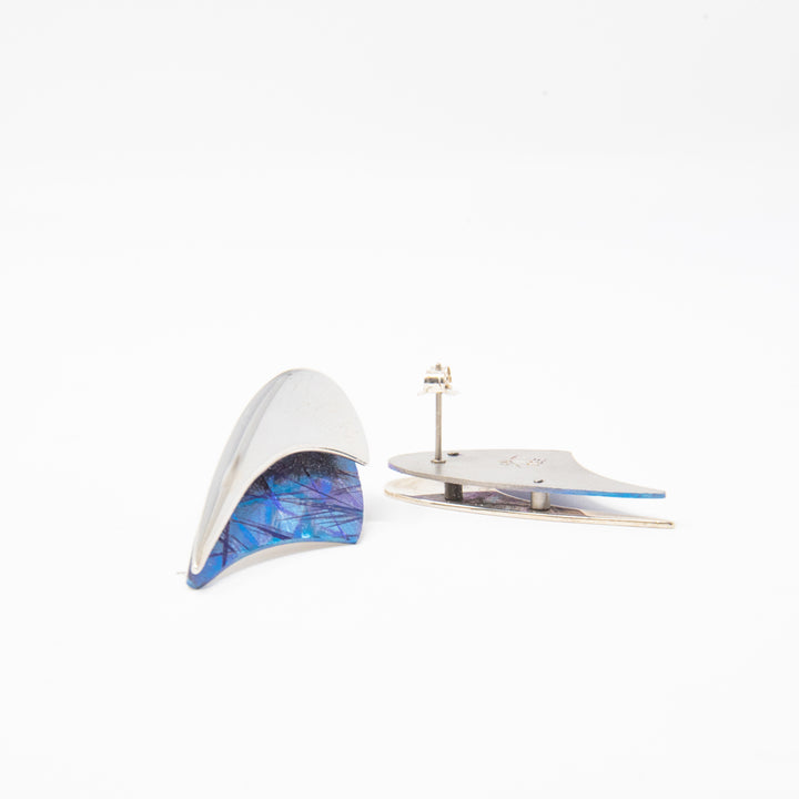 These unique titanium stud earrings are made form sterling silver and anodized titanium. The tops of the earrings are made from a silver band that warps around crescent shaped pieces of titanium. The titanium is blue and has colorful designs on it achieved by anodizing the metal.