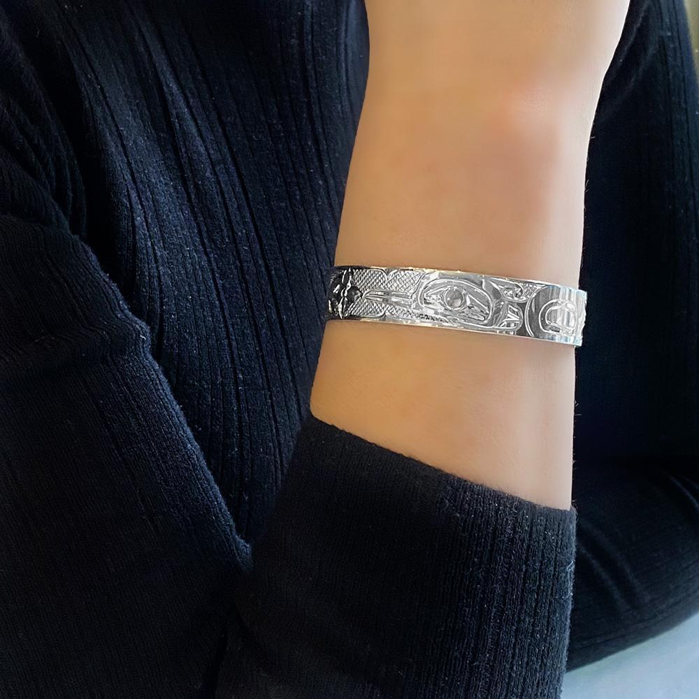This Hummingbird bracelet is made from sterling silver and has a single band with a gap in the back. There is a depiction of the Hummingbird among flowers carved into the surface of the band.