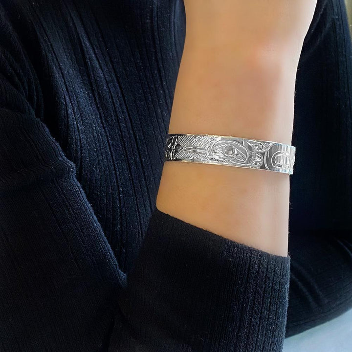 This Hummingbird bracelet is made from sterling silver and has a single band with a gap in the back. There is a depiction of the Hummingbird among flowers carved into the surface of the band.