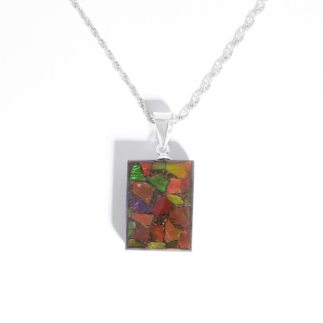 Pendant by Aryn Bowers. He has encased flakes of ammolite in resin to create it. Double-sided, each side has a unique display of ammolite. Sterling silver bail. Pendant measures 1" x 0.5" including bail.