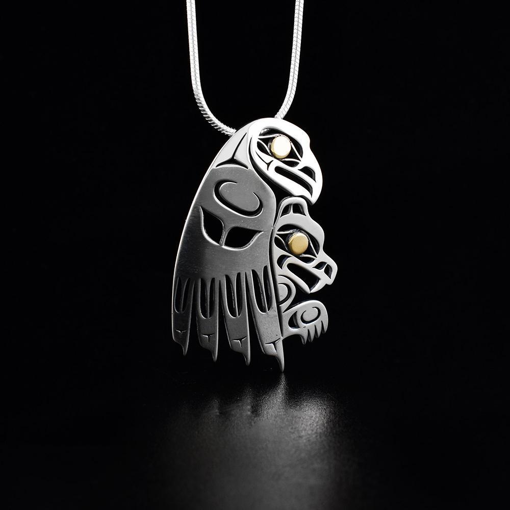 This Bear and Eagle pendant is made from sterling silver and 18K gold. The piece is shaped like and has cutout designs that depict the Eagle carrying the Bear and their eyes are made from gold.